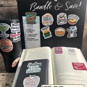 May include: A collection of stickers, a tumbler, a notebook, and an open book. The stickers have various designs and phrases, including "Make it a Great Day" and "Emotional Support Chips & Queso." The tumbler has stickers. The notebook says "Healing & Still Worthy."