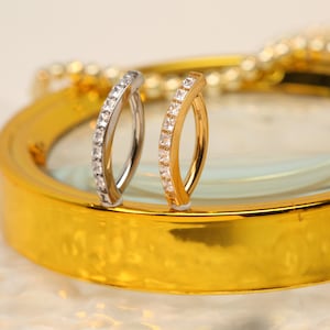 May include: Two silver and gold hoop earrings with a row of clear cubic zirconia stones.