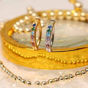 Puede incluir: Un par de pendientes de aro arcoíris con acabado plateado y dorado. Los pendientes están engastados con pequeñas piedras preciosas de colores.