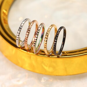 May include: Six different colored nose rings with a textured, diamond-shaped pattern. The rings are made of stainless steel and are available in silver, rose gold, rainbow, gold, black, and gunmetal.
