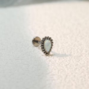 Puede incluir: Pendiente plateado en forma de lágrima con un centro de ópalo blanco y un borde con cuentas. El pendiente tiene una parte trasera plana y un poste para perforar. Joyería para piercing.
