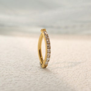 May include: A gold hoop earring with a row of clear cubic zirconia stones.