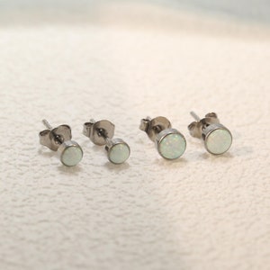 May include: Three pairs of silver stud earrings with white opal stones. The earrings are arranged in order of size, with the smallest on the left and the largest on the right.