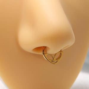 May include: Gold nose ring with an alien face design. The ring is in the shape of a heart.