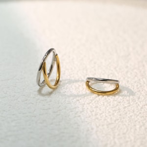 Op de afbeelding: Twee eenvoudige ringen, een zilveren en een gouden, worden getoond op een wit oppervlak. De ringen zijn beide dun en hebben een afgeronde vorm.