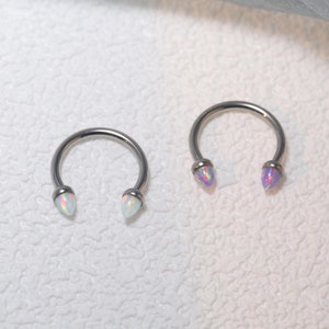 Puede incluir: Dos anillos de plata en forma de herradura con piedras que parecen ópalos en los extremos. Un anillo tiene piedras blancas y el otro tiene piedras moradas.