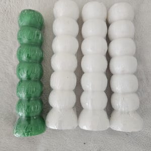 May include: An assortment of decorative candle holders. One green candle holder is next to three white candle holders. Each candle holder has a stacked, rounded design. The candle holders are on a light gray surface.