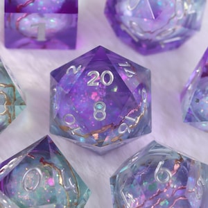 Peut inclure: Gros plan sur plusieurs dés polyédriques. Les dés sont d'un violet translucide avec des reflets dorés et des paillettes. Le dé au centre affiche le chiffre 20. Les dés sont utilisés pour les jeux de société.