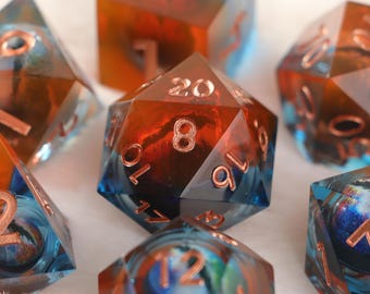 May include: A collection of polyhedral dice with a striking design. The dice feature a combination of blue and orange resin with copper-colored numbers. The dice are in various geometric shapes, including a twenty-sided die.
