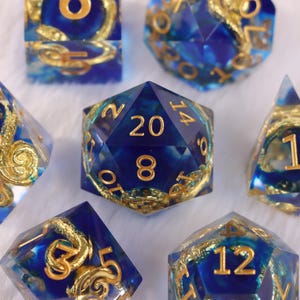Puede incluir: Un conjunto de dados poliédricos azules y dorados. Los dados transparentes presentan remolinos y números dorados. El dado más grande muestra el número 20. Diseñados para juegos de rol de mesa.