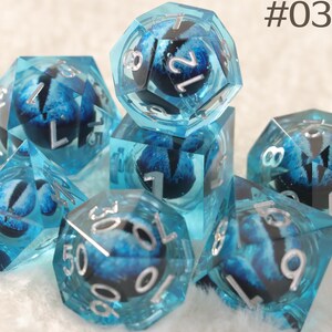 K&ouml;nnte beinhalten: Ein Satz polyedrischer W&uuml;rfel aus transparentem blauem Harz. Jeder W&uuml;rfel zeigt ein detailliertes blaues und schwarzes Augendesign im Inneren, mit silbernen Zahlen. Der Text "#03" ist ebenfalls enthalten.
