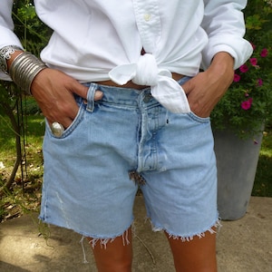 Peut inclure: Une femme portant une chemise blanche boutonnée nouée à la taille et un short en jean bleu clair avec des bords effilochés.