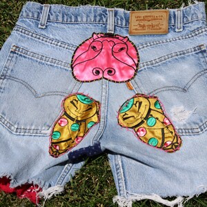 May include: Light blue denim shorts with a pink hippopotamus, gold and green butterfly, and red and white polka dot fabric patches sewn on.