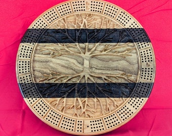 May include: A wooden cribbage board with a tree of life design. The board has a black and brown striped pattern and is made of wood. The board has a circular shape and is approximately 12 inches in diameter.