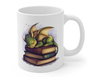 Op de afbeelding: Witte keramische mok met een illustratie van een groene draak die slaapt op een stapel boeken. De draak heeft gele vleugels en hoorns. De boeken zijn bruin en blauw. De mok heeft een gebogen handvat.