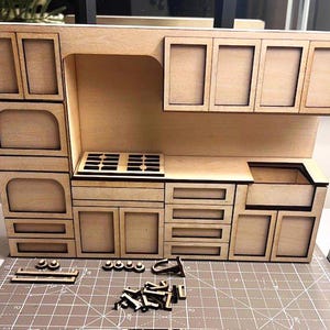 Könnte beinhalten: Ein Miniatur-Küchenset aus Holz mit Schränken, einer Spüle und einem Herd. Das Set ist aus unbehandeltem Holz und kann bemalt oder gebeizt werden.