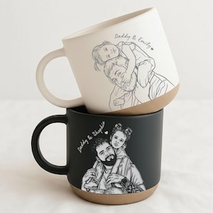May include: Two ceramic mugs, one cream and one black, stacked. Each mug features a sketch of a father with a child on his shoulders. The cream mug has the text "Daddy & Emily". The black mug has the text "Daddy & Sophia".
