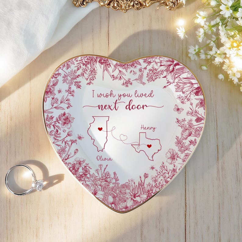 May include: Heart-shaped trinket dish with a floral design and gold trim. The dish features the text "I wish you lived next door" and illustrations of the states of Illinois and Texas, with names and hearts. A diamond ring is in the foreground.