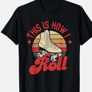 May include: Black t-shirt featuring a retro design with a roller skate graphic. The text "THIS IS HOW I Roll" is in red, with a colorful sunset-style background. A star is on each side of the text "THIS IS HOW I".