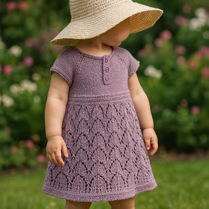 Könnte beinhalten: Ein lavendelfarbenes Strickkleid mit Blattmuster und kurzen Ärmeln. Das Kleid hat drei kleine Knöpfe am Halsausschnitt. Ein beiger Sonnenhut mit breiter Krempe wird zu dem Kleid getragen. Das Kind steht auf grünem Gras.
