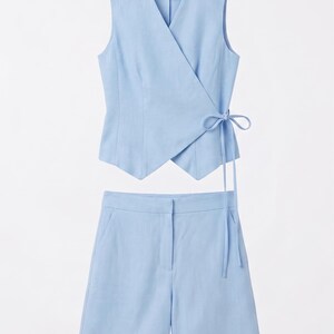May include: A light blue two-piece outfit. The top is a wrap-style vest with a tie closure. The matching shorts have a tailored fit. The set is made of a lightweight fabric, perfect for warm weather.