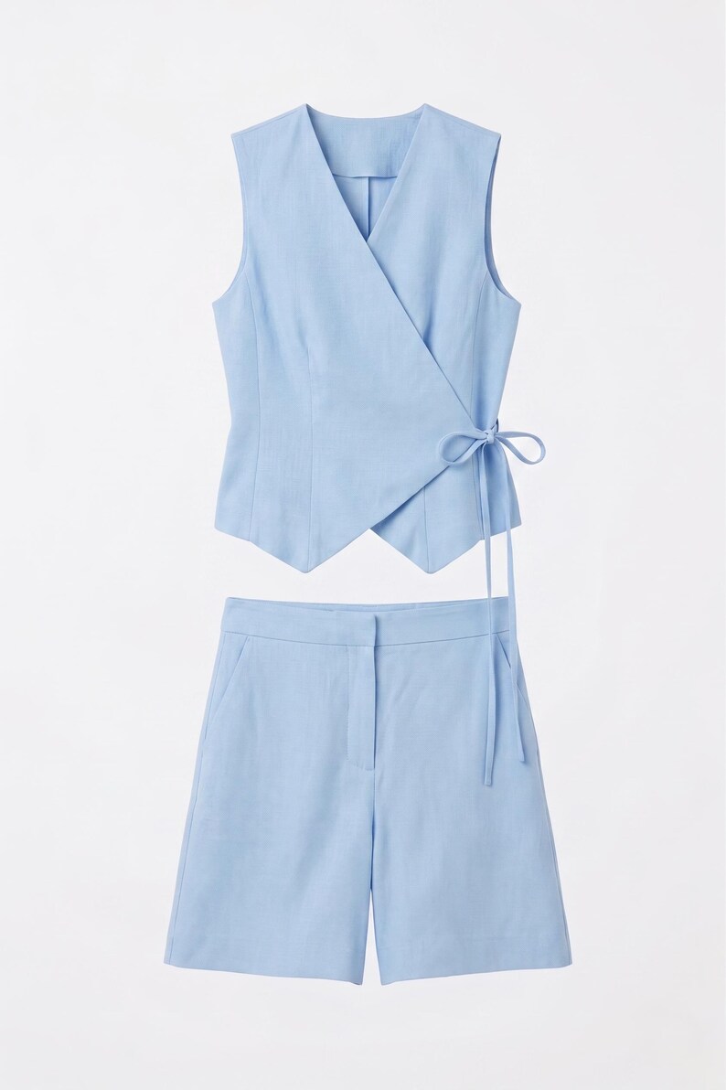 May include: A light blue two-piece outfit. The top is a wrap-style vest with a tie closure. The matching shorts have a tailored fit. The set is made of a lightweight fabric, perfect for warm weather.