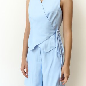 May include: A light blue sleeveless wrap top and matching shorts set. The top features a V-neck and tie closure. The shorts are high-waisted. The outfit is made of a smooth, solid-colored fabric.