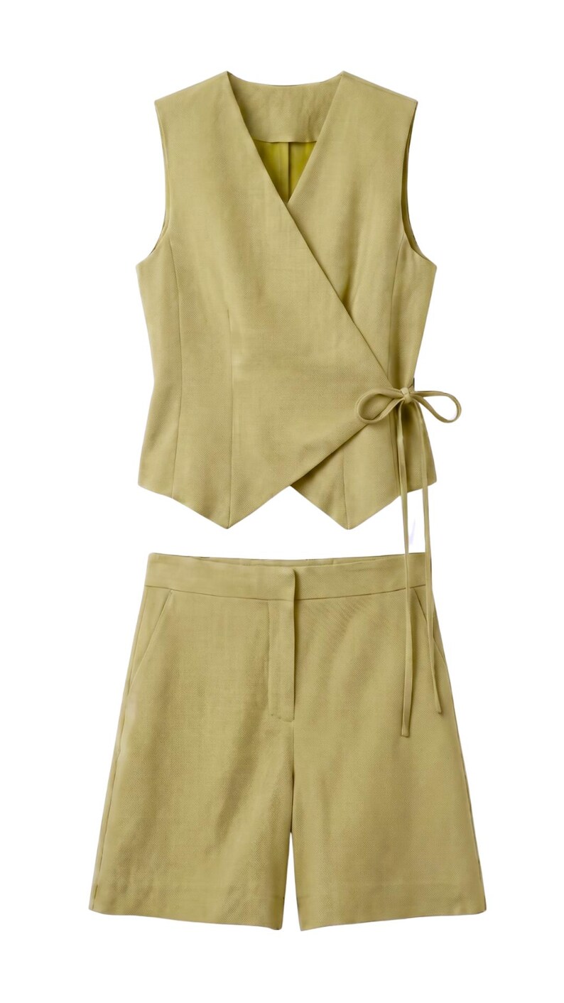 May include: A two-piece outfit in a light olive green color. The set includes a sleeveless wrap top with a tie closure and matching shorts. The fabric appears to be linen or a similar lightweight material, suitable for warm weather.