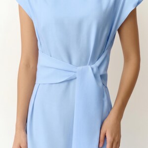 May include: A pale blue dress with short sleeves and a matching waist tie. The dress has a knotted detail at the waist. The fabric looks smooth and lightweight. The dress is a simple, elegant design.