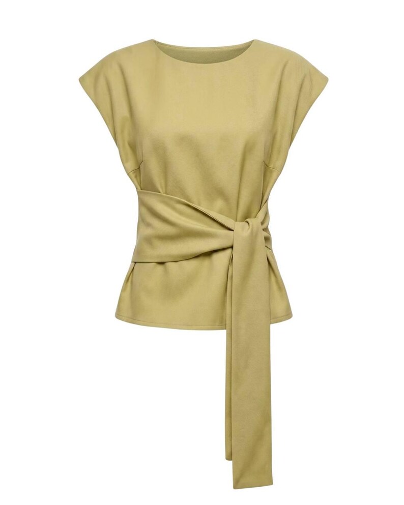 Puede incluir: Top de color verde oliva claro con una cinta envolvente en la cintura. La parte superior tiene mangas cortas y un cuello redondo. La corbata cuelga hacia abajo en el lado derecho. La tela parece ser un material suave similar al ante.