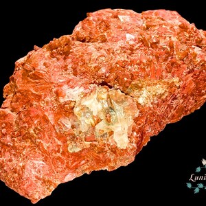 Pode incluir: Um espécime mineral áspero, vermelho-alaranjado, com uma estrutura cristalina. A rocha tem uma seção mais clara e translúcida no centro. O fundo é preto. O texto "LuniNature" está no canto inferior direito.