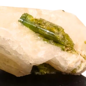 May include: A clear quartz crystal with a green tourmaline crystal embedded inside. The quartz is translucent and has a slight pink hue. The tourmaline is a deep green color and has a glassy luster.