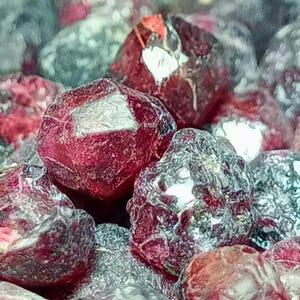 Pode incluir: Close-up de um monte de pedras preciosas vermelhas com um acabamento brilhante e metálico. As pedras têm uma forma irregular e uma textura áspera.