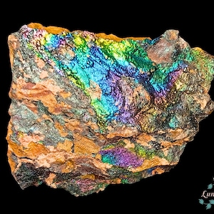 Puede incluir: Un espécimen mineral rugoso e iridiscente con un espectro de colores que incluye azul, verde, amarillo y morado. La roca tiene una superficie texturizada y está sobre un fondo negro. El mineral parece ser un tipo de pirita.