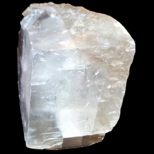 May include: A large, clear, translucent crystal with a cubic shape. The crystal has a slightly cloudy appearance and is likely a natural mineral specimen.