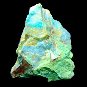 Può includere: Primo piano di un campione minerale colorato su sfondo nero. La roccia presenta un mix di tonalità verdi, blu e gialle, con alcune aree che mostrano macchie rosso-brunastre. La consistenza appare ruvida e naturale.