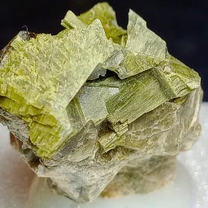 Pode incluir: Um aglomerado de cristais verdes e cinzentos com uma superfície áspera e texturizada.