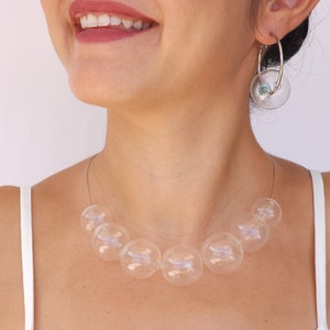 May include: A clear glass bubble necklace with a silver chain. The necklace is made of multiple large, round glass bubbles.
