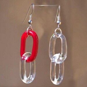 May include: A pair of earrings featuring a chain link design. One earring has a red link connected to a clear link. The other earring has two clear links. The earrings have silver-colored ear wires.