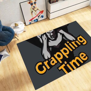 May include: A rectangular grey rug with the words "Grappling Time" in orange and black. The rug features a stylized illustration of a muscular figure in a grappling pose. The rug is on a wooden floor.