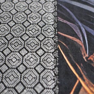 May include: Close-up of a black and white fabric with a geometric pattern. The fabric has a textured surface and a subtle sheen. The pattern is made up of small squares and circles.