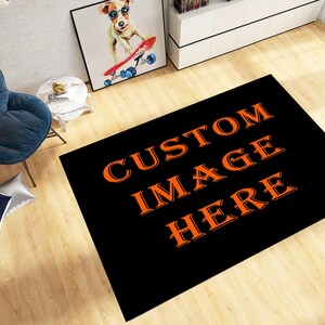 May include: A black rectangular rug with the words "CUSTOM IMAGE HERE" in orange. The rug is on a wooden floor, with a blue chair and a framed picture of a dog in sunglasses in the background.