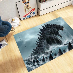May include: A rectangular rug with a detailed illustration of Godzilla rising from the ocean. The rug has a blue and grey colour scheme, with a dramatic depiction of the monster and crashing waves. The rug is placed on a wooden floor.