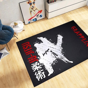 May include: Black rectangular rug featuring a white graphic of two figures in a grappling position. The words "JIU-JITSU" and "GRAPPLING" are in red, with Japanese characters below. The rug is on a wooden floor.