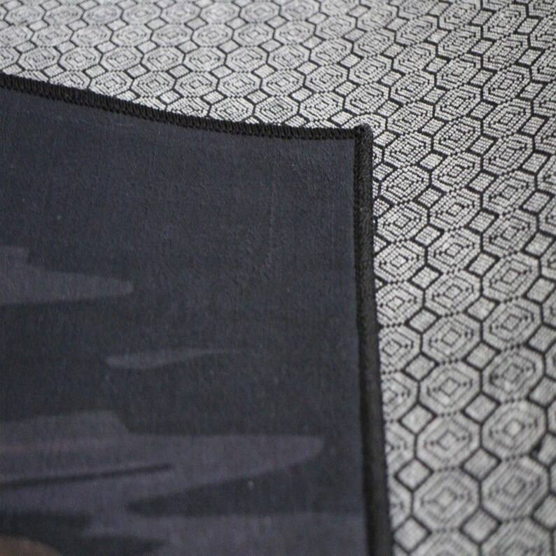 May include: Close-up of a black fabric with a subtle pattern of gray clouds. The fabric has a black stitched border.