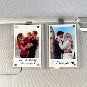 May include: Two clear acrylic photo holders with metal clips. Each holder displays a photograph. One shows a family, the other a couple. Text on the first reads "Drive Safe, Daddy! We love you!" The second says "I Love you."