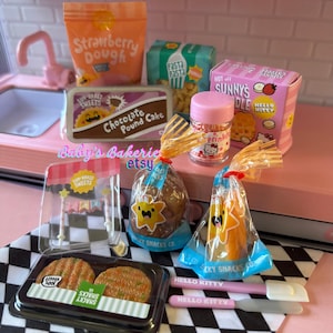 May include: A collection of miniature toy food items, including a package of strawberry dough, pasta, a chocolate pound cake, and a pink Hello Kitty box. Other items include a jar of sprinkles, and packaged snacks. The theme is a miniature bakery.