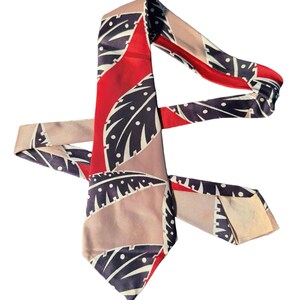 May include: A patterned tie with a design of stylized leaves in navy, white, and red. The tie has a red central stripe and sections of tan and light pink. The tie is made of a smooth material, possibly silk.