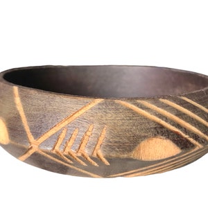 May include: A dark brown wooden bowl with a geometric design carved into the surface. The design features light brown lines and shapes.