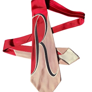 May include: A vintage necktie with a striking design. The tie has a red background with a large, stylized "R" in red, black, and cream. The tie's body is a light tan colour. The tie is made of a shiny material.